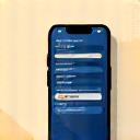 Ikona mobilného telefónu s bankovou aplikáciou v rôznych jazykoch, symbolizujúca multijazyčné digitálne platformy.